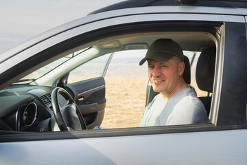 handsome mature man sits behind the wheel in his car in nature on a sunny day