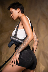 tattooed archaeologist with short hair and crop top standing in holster with gun.