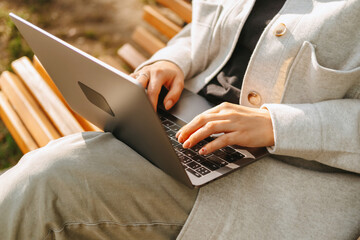 Close up photo of female hands typing on the laptop while sitting on a bench.