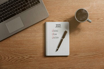 Naklejka premium Notebook with an action plan for the year 2023, a laptop and a hot coffee - concept propositions and action plan, new year