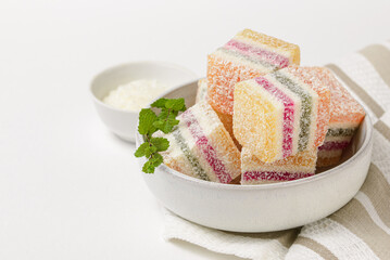 Multi-colored striped marmalade with with coconut topping in a light ceramic plate on a striped table napkin isolated