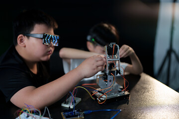 A cute boy constructs metal robot and program it boards microcontrollers on the table STEM education inscription. Programming Mathematics The science Technology DIY workshop at class in the classroom