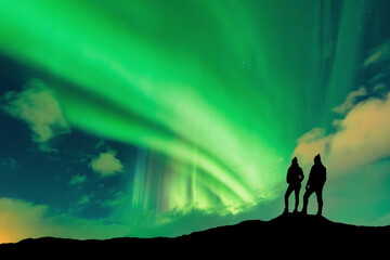 A silhouette of young adventurous couple watching the northern lights also known as aurora borealis. High quality photo - 543426154
