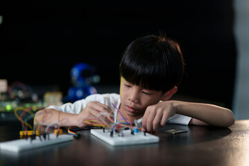 A cute boy constructs metal robot and program it boards microcontrollers on the table STEM education inscription. Programming Mathematics The science Technology DIY workshop at class in the classroom