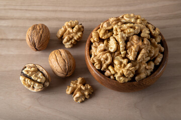 Peeled walnuts and whole walnuts in wooden bowl
