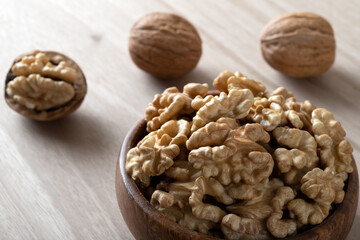 Peeled walnuts and whole walnuts in wooden bowl