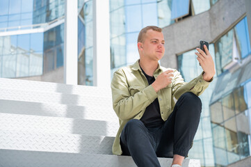 Young man sitting on the stairs and talking sign language via video link on smartphone outdoors. 