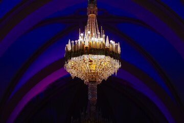 Elegant luxury crystal chandeliers on ceiling in purple and blue light. Emphasis on luxury, used in various places such as palace church, residence. Decorative elegant vintage and Contemporary Concept