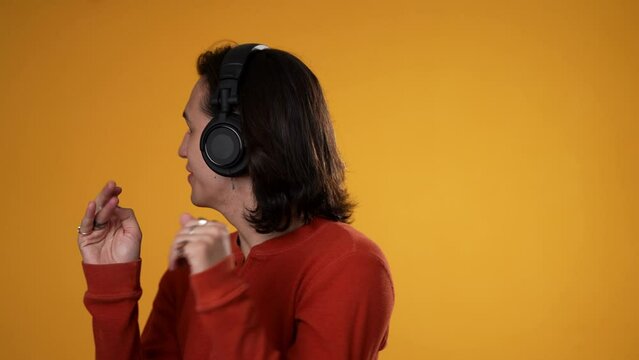 Slow motion portrait of happy smiling dancing Hispanic Latino gender fluid non-binary man wearing headphones isolated on yellow background.