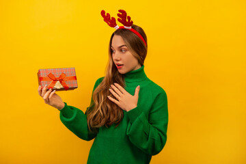 Surprised shocked brunette girl holding wrapped present, keeping hand on chest and looking at gift...