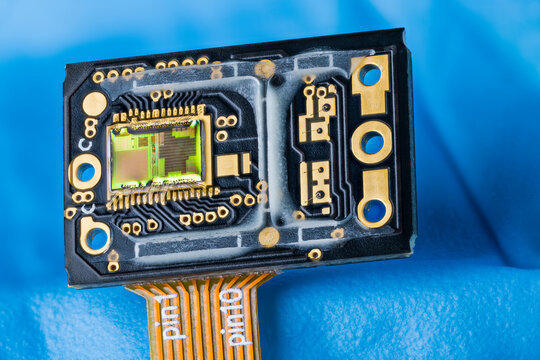 Optoelectronic image sensor of optical laser computer mouse on a blue background. Modern green silicon die with photodiodes array and gold wires on dark PCB with orange flexible printed circuit cable.