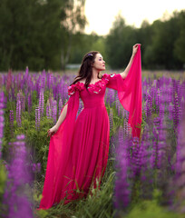 Beautiful girl in long pink dress  stading in flower field. Fantasy woman portrait in lupin flowers