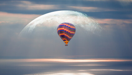 Multi colored hot air balloon flying over the sea full moon in the background at sunset 