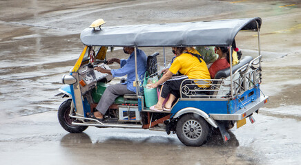 A traditional motor tricycle - tuk tuk full of passenger rides in a rain, Thailand