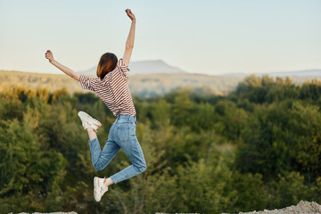 Happy woman jumping up from happiness in nature with her back to the camera with a beautiful...