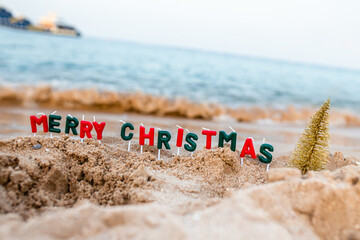 Christmas Eve. An inscription of candles Merry Christmas and a Christmas tree on the sand. New...