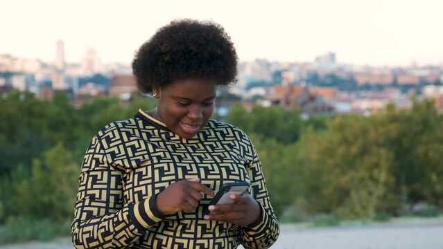 Young Equatoguinean woman laughing while using the smartphone at street.