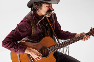 Portrait of man with moustaches in country style clothes playing guitar and harmonica, live...