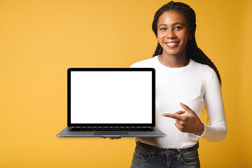 Satisfied multiracial woman advertising new computer app isolated on yellow background, mock-up....