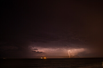 A large lightning bolt opened up at night on the sea horizon next to the ship, illuminating the cloudy sky with light.	
