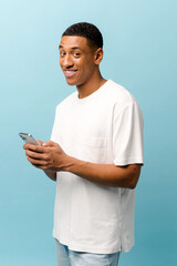 Vertical portrait of cheerful African-American man in white t-shirt using cellphone and smiling,....