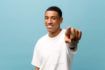 Attractive cheerful young african-american guy wearing white casual t-shirt points index finger at...