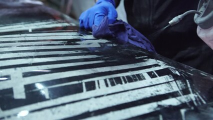 Man worker sanding car hood body element in auto service workshop