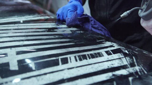 Man worker sanding car hood body element in auto service workshop