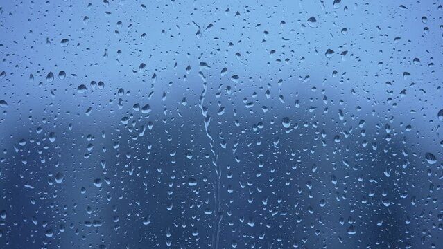 Raindrops on a blue background dripping down the window close-up