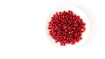 Ripe pomegranate grains in a white plate isolated on a white background. Top view, flat lay.