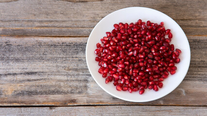 Ripe pomegranate grains in a white plate isolated on a wooden background. Top view, flat lay.