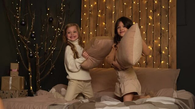 The girls are playing pillows on the bed, with a Christmas decoration. Socializing, chatting and sisters or younger children gossiping at a fun pajama party or sleepover