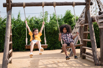 Happy Asia and African American kids girl play swing on play ground in the park	
