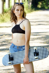 Beautiful young woman with skateboard outside in nature on a summer day