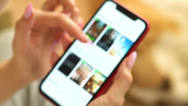 Young woman sitting down on sofa in living room at home searching for film or TV series to watch for leisure. Choosing movie on internet streaming service. Blur focus