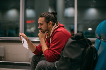 A very upset, confused young man with tickets in his hands at the airport gate at night.  Flight...