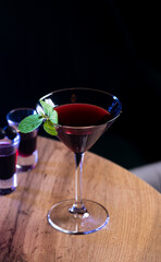 Red cocktail in a triangular glass decorated with a mint leaf.