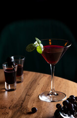 Red cocktail in a triangular glass decorated with a mint leaf.