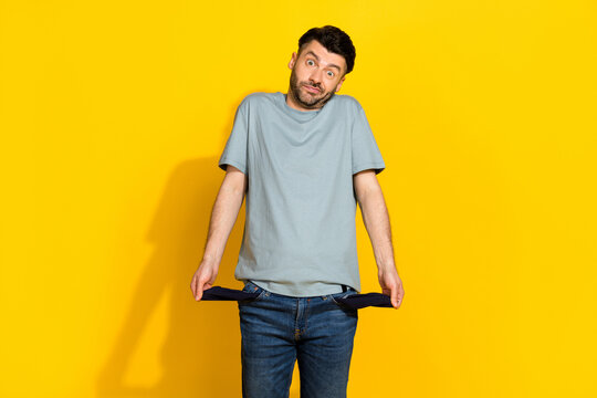 Photo of young funny excited stressed man frustrated confused problems showing his empty pockets poverty no money isolated on yellow color background