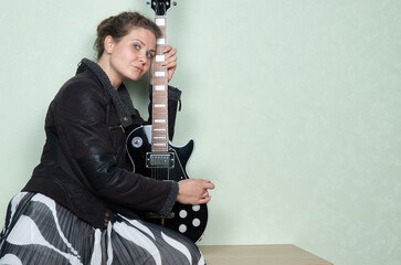 Woman with curly hair in leather jacket playing black electric guitar
