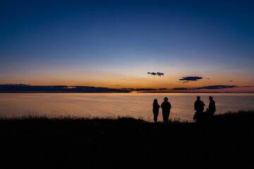 Silhouette of group of friends watching beautiful sunset at ocean.