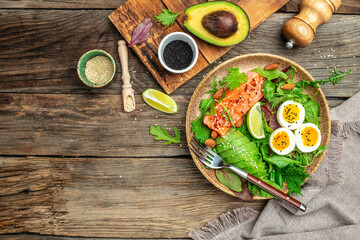 Fototapeta na wymiar Salted salmon salad with fresh green lettuce, grape, eggs and avocado. Ketogenic, keto or paleo diet lunch bowl. Top view