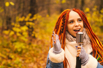 Young woman with bright hairstyle with retro microphone in autumn forest. Portrait of female singer...