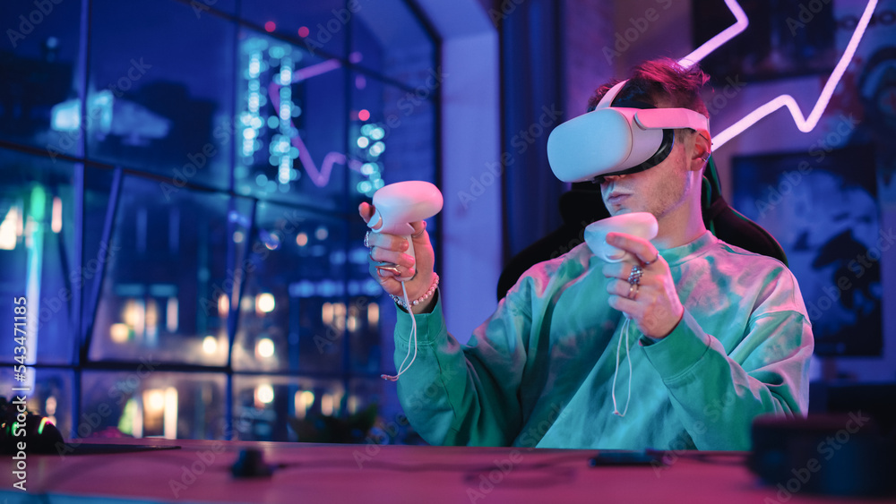 Poster fashionable man using virtual reality equipment with controllers at home in loft apartment. young ma