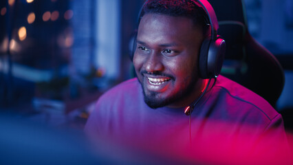 Successful Gamer Winning in Online Video Game on Computer. Portrait of Young Black Man in Headphones Playing PvP Tournament with Other Professional Players, Talking with Team on Microphone. © Gorodenkoff
