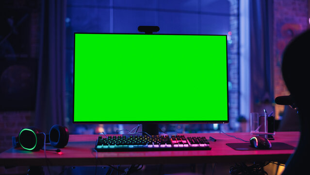 Gaming at Home: Empty Gamer Station with Player's Personal Computer with Green Screen Chroma Key Display Standing on a Wooden Desk in Cozy Loft Apartment with Neon Lights. 