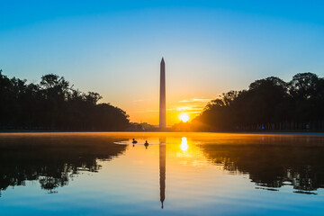Colorful sunrise behind the Washington Monument with reflections in the reflecting pool with ducks...