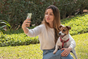Woman and Jack Russell dog taking selfie with the cellphone at the park during a warm sunny day