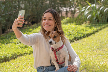 Woman and Jack Russell dog taking selfie with the cellphone at the park during a warm sunny day