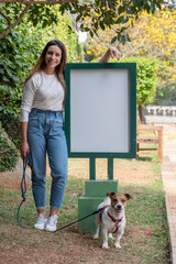 Woman and Jack Russell dog posing by a blank sign at the park during a warm sunny day